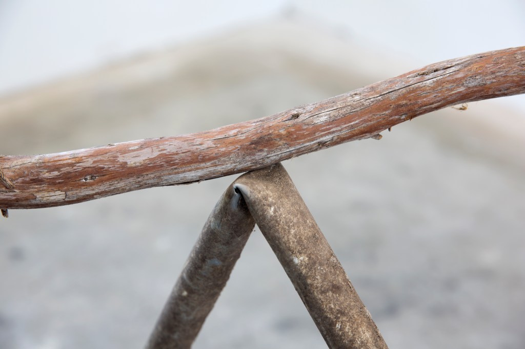 A wooden branch rests on a bent metal tube.