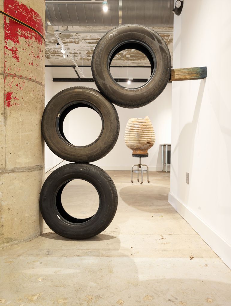 Three tires stacked and wedged between two walls with a wooden block.