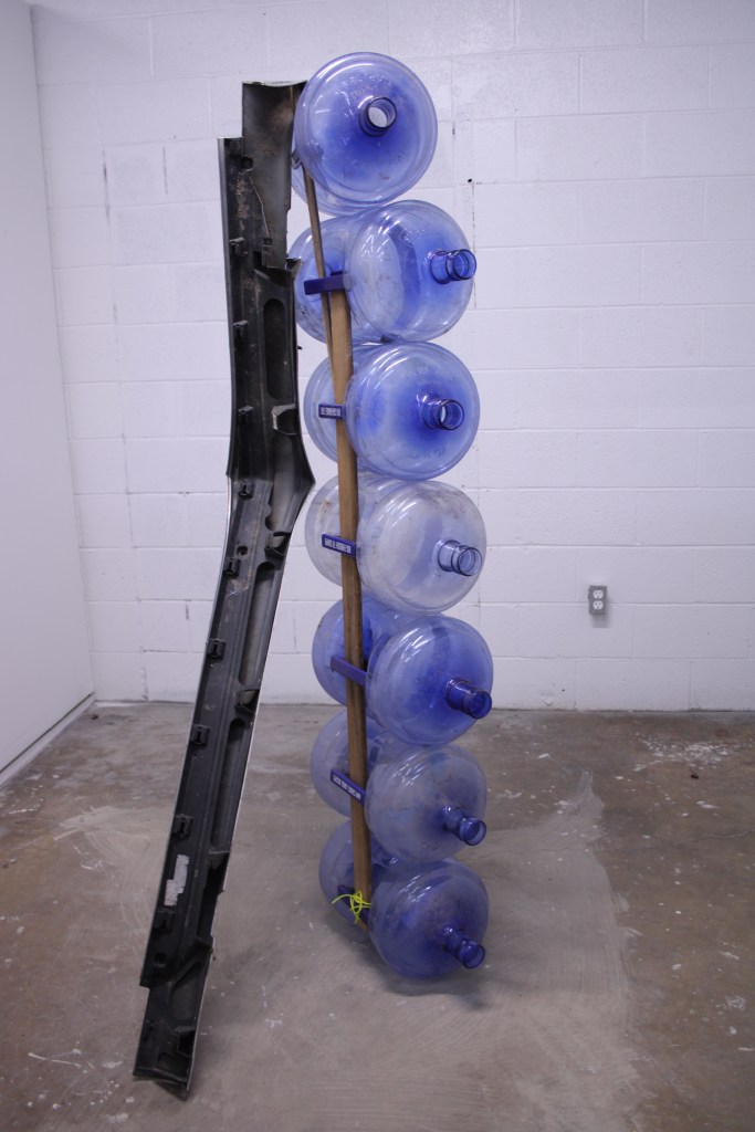Water jugs on their sides stack are stacked vertically, a plastic beam props it in place.