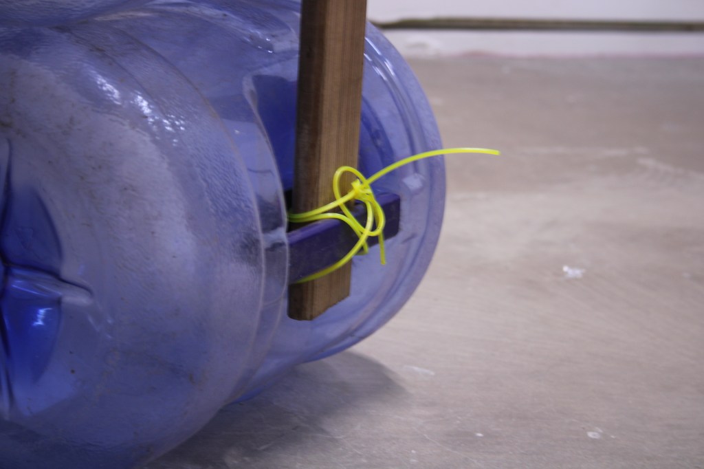 Wooden beam hold by empty water jug and fluorescent string.