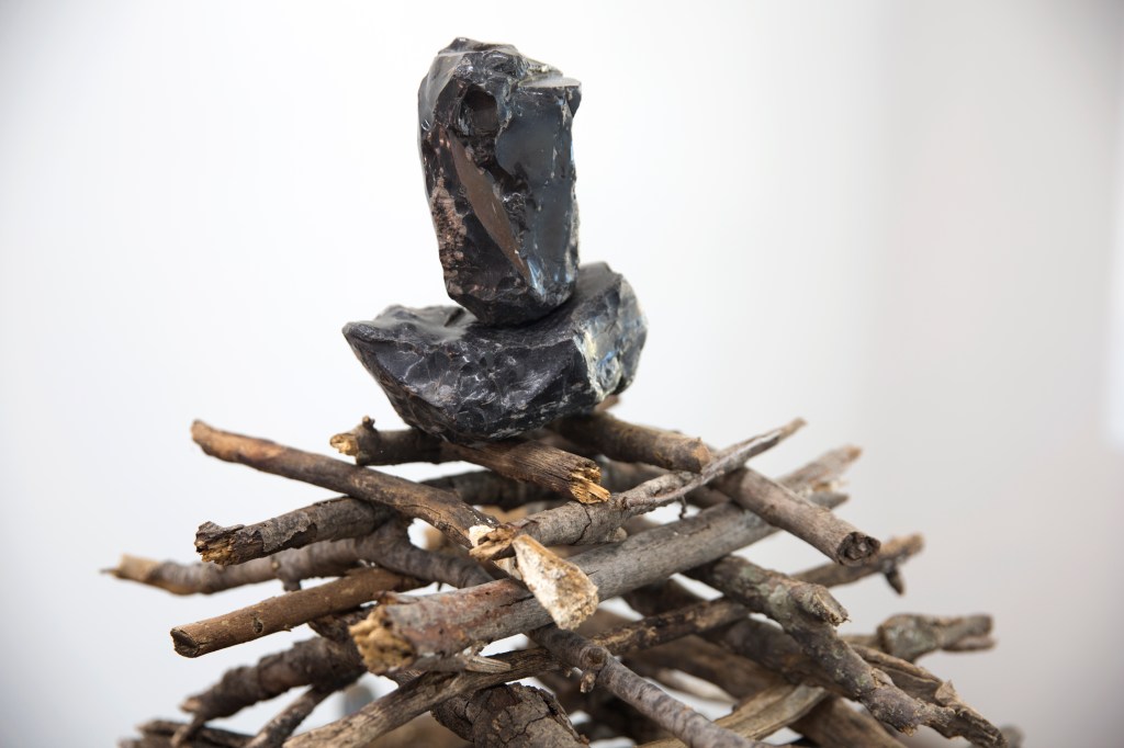 Two sheared stones balanced on a lattice of branches.